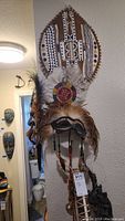 Front view of the large feathered ritual mask mounted on a wall with intricate beadwork and geometric patterns