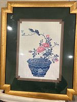 Framed fabric wall art showing detailed floral and bird design with gold colored frame and green matting.