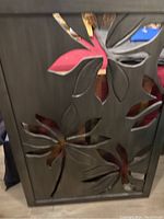 Front view of the metal wall art showing floral and leaf cutout details and dark finish.