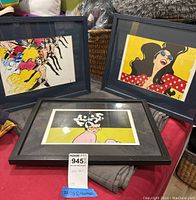 Three framed wall art prints placed on a table, showing colorful illustrations of women in stylized artistic form.