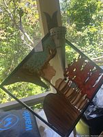 Photo of one metal square wall art piece with layered, rust-tone design mounted on a vertical post against greenery background