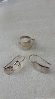 Photo of the hand-made 925 silver ring with hammered texture and the pair of matching earrings showing the front side with curved and textured surfaces.