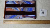 Top view of the fused glass tray showing its multicolored swirl design in blue, brown, white, and orange along with its rectangular segmented form and artist signature.