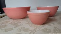 Three pink Pyrex mixing bowls of varying sizes arranged on table