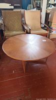Round teak coffee table with radial grain pattern, two chairs in background