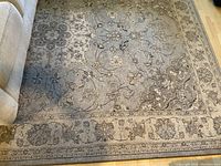 Full view of the 11'x8' area rug showing traditional floral pattern with cream, grey, and blue colors, laid on hardwood floor near sofa.