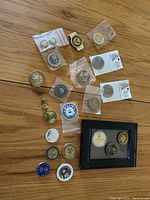 Overview of coin lot showing various challenge coins, some loose and some in plastic sleeves, plus a black framed set of three coins.