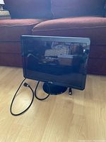 Front view of Dell computer monitor showing screen and round base stand with attached power cable on wooden floor.