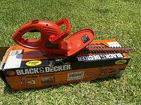Orange Black & Decker electric hedge trimmer positioned on top of its original box outdoors on grass.