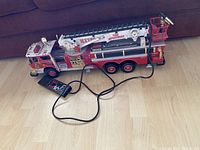 Full side view of a large red and white vintage firetruck toy with wired remote control on hardwood floor.