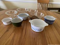 Photo showing the full set of 11 assorted used glass mixing bowls on wooden table with chair in background