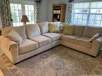 Full view of the light tan L-shaped sectional sofa in a living room setting, showing overall condition and fabric texture.