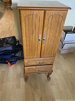 Front closed view of the tall wooden jewelry chest showing two doors, two lower drawers, and curved legs.