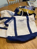 Two medium white canvas tote bags with blue trim and Mirabelle embroidery, shown laid flat on a table.