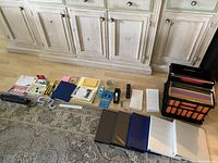 Multiple school and office supplies laid out on the floor including binders, file organizers, and other stationery items.