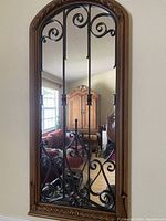 Front view of the tall wall mirror showing wooden arched frame, metal scrollwork bars, and reflective glass.