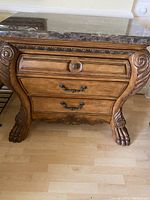 Front view of wood chest showing ornate drawer handles, claw feet, scroll carvings and marble top.