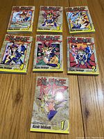 Photo of 7 Yu-Gi-Oh manga volumes laid out on a wooden floor, showing the front covers numbered 1 through 7.