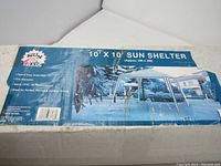 Box showing packaging of 10' x 10' sun shelter, blue box with product image and information