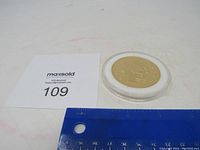 Photo showing replica gold coin in plastic case next to a ruler for size reference.