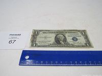 1935 D Blue Seal $1 Silver Certificate laid flat with ruler alongside for size reference; some wear and creasing visible.