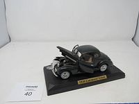 Full side view of the black 1939 Chevrolet Coupe model car with hood open revealing engine details, displayed on a black base with label.