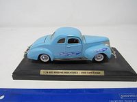 Front side view of light blue 1:24 scale model 1948 Ford Coupe showing detailed purple and white flame decals and chrome wheels, mounted on display base.
