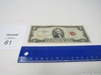 Front side of the 1963 red seal $2 bill placed alongside a blue ruler for size reference.
