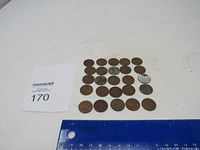 25 old wheat pennies arranged in rows alongside a ruler for size scale, showing mostly brown patina surface.