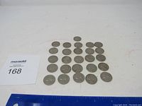 Lot of 26 old circulated nickels arranged on white surface, showing general wear consistent with use and age.