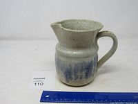Front angled view of the ceramic pitcher showing its handle, spout, and blue drip glaze decoration with a ruler for size reference.