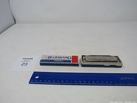 Harmonica and original branded case placed next to a ruler for scale.