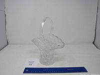 Full view of the clear glass basket with handle placed on a white surface with a blue ruler nearby for scale.