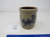 Front view of the beige crock featuring the blue floral and scroll design, showing the shape and condition of the item.