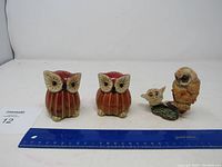 Three owl figurines displayed with ruler for scale: two identical red and cream owls with large eyes, and one brown adult owl with baby owl on branch.
