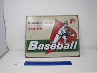 Front view of rectangular metal sign featuring Topps baseball bubble gum advertising with a baseball player and text reading 'Bubble Gum Topps Baseball 1¢'. The sign shows signs of wear including rust and discoloration.