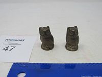 Two small brass or bronze owl figurines side by side with a ruler showing size.
