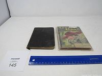 Two vintage books side by side; one leather-bound with a worn black cover, other with colorful illustrated dust jacket titled 'Adree Le Roy'