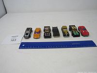 Front view of all 7 vintage diecast cars in a line with ruler for scale, showing used condition and size variation.