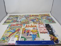 Photo showing seven vintage comic books including Archie, Jughead, and X Force titles laid flat with ruler for scale.