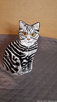 Front view of black and white striped ceramic cat figurine with yellow eyes, sitting posture, detailed face.
