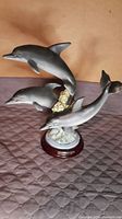 Overview photo showing the three dolphin figures mounted on a coral-like base and wooden platform.