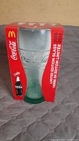 Front view of the Coca Cola 2015 limited edition glass in original red and white McDonald's branded box, showing embossed logo and text on glass.