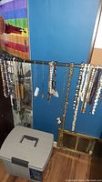 Full view of multiple necklaces and chains hanging on a horizontal bar, showing variety of styles and materials including metal chains and beaded jewelry.