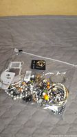 Plastic bag containing assorted costume jewelry including bracelets, earrings, and beaded necklaces all in one group on a quilted grey surface.