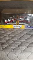 Image of collectible die cast metal vehicles in original display box on quilted surface showing overall set and packaging condition.
