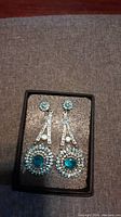 Photo of the earrings laid flat in a black box showing detailed design and crystals