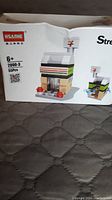 Photo of the Hsanhe building block set packaging showing front with markings of 55 pieces, age 6+, model 2000-3 and image of the assembled 7-Eleven block store.