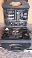 Open black plastic carrying case showing organized tool set including hex keys, screwdrivers, spirit level, pliers, tape measure, and screwdriver.