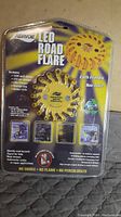 Front packaged view of Aervoe LED Road Flare showing a yellow circular solar road flare with product info and hazard warnings on the packaging